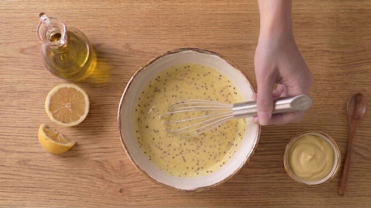 Preparazione del dressing al limone e senape con frusta, olio e ingredienti freschi.